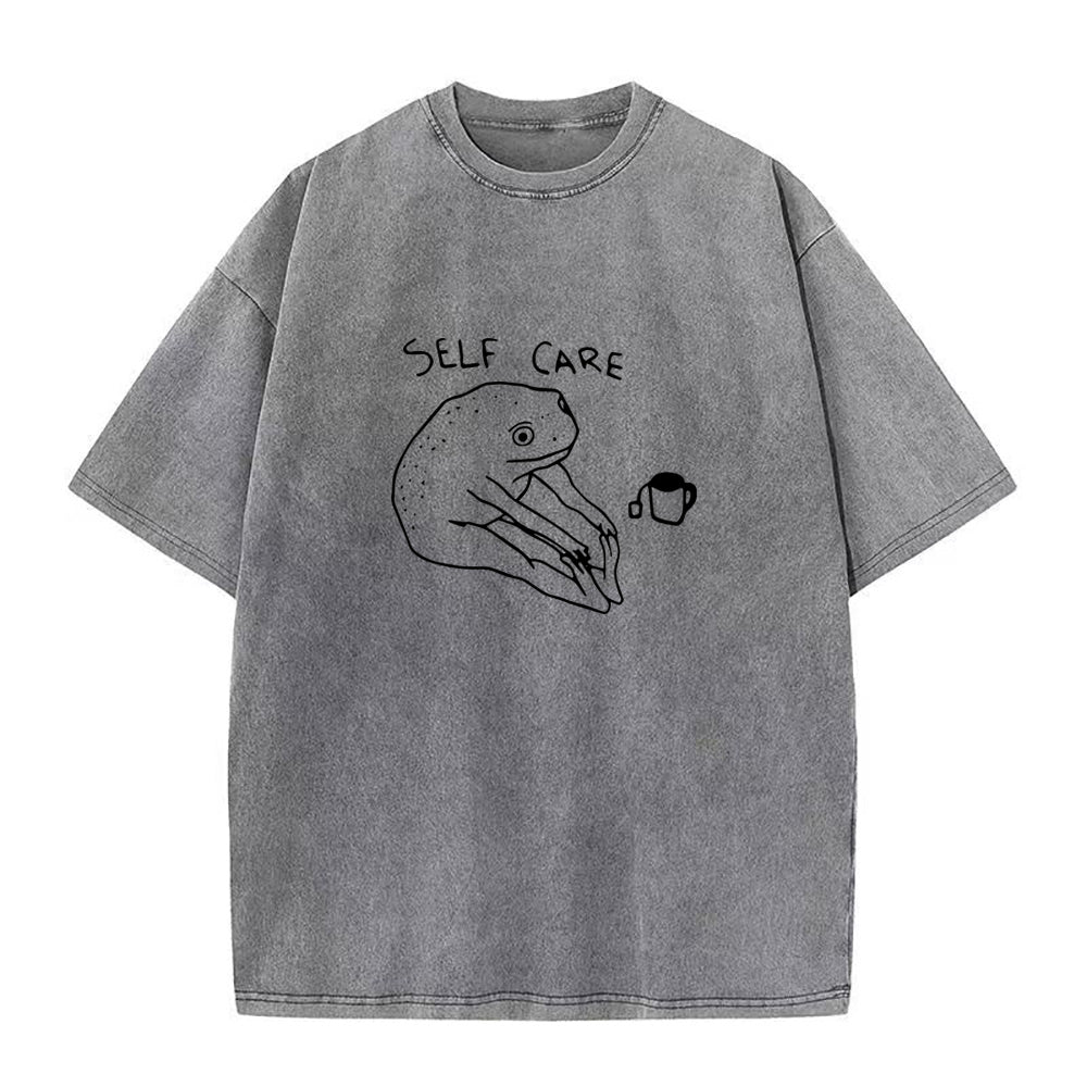 Gray t-shirt with 'self care' and hand holding a cup illustration on a white background